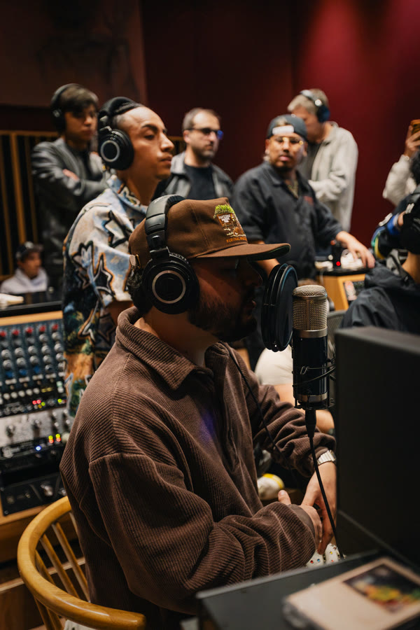 Productor con audífonos frente a la consola, artistas detrás